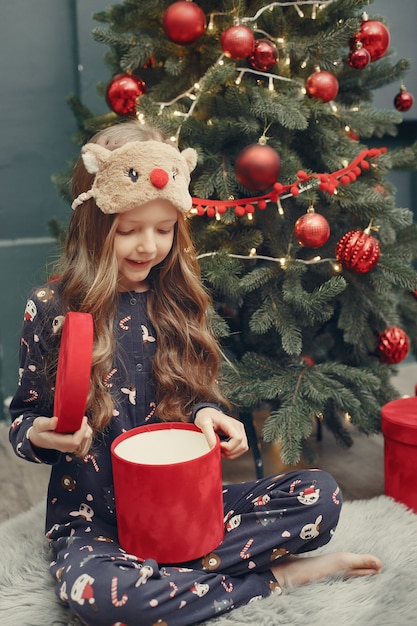 Petite fille près de sapin de Noël en pyjama bleu