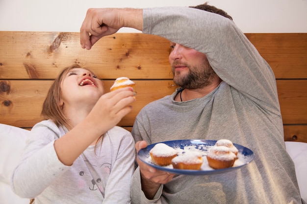 Petite fille qui mange des muffins avec son père au lit