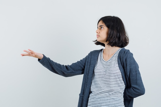 Petite fille qui s'étend de la main de manière interrogative en t-shirt, veste et à la confusion