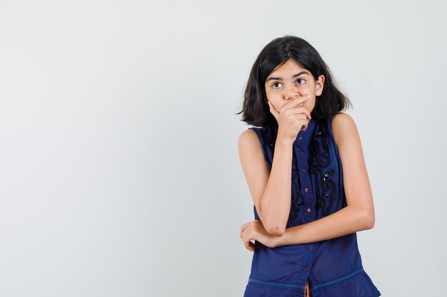 Petite fille regardant avec la main sur la bouche en chemisier bleu et à la pensif.