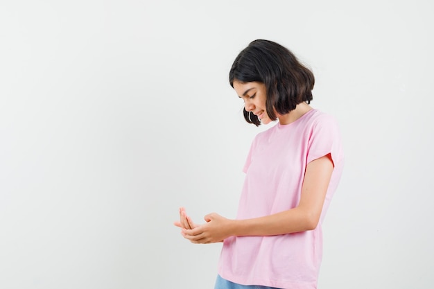 Petite fille regardant sa paume en t-shirt rose, short et espoir, vue de face.