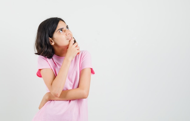 Petite fille regardant en t-shirt rose et à la rêveuse, vue de face.