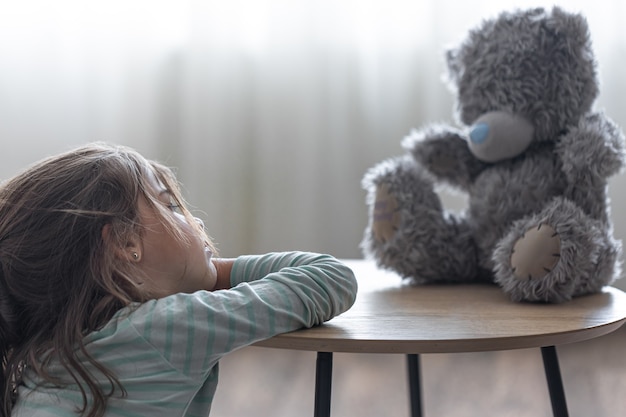 Photo gratuite petite fille regarde son ours en peluche, un enfant avec un jouet préféré sur un espace de copie d'arrière-plan flou.