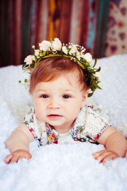 Une petite fille rêveuse avec une couronne rose sur les cheveux dorés se trouve sur une couverture moelleuse