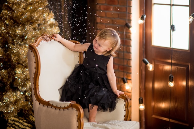 Petite fille en robe noire se trouve parmi les décorations de Noël