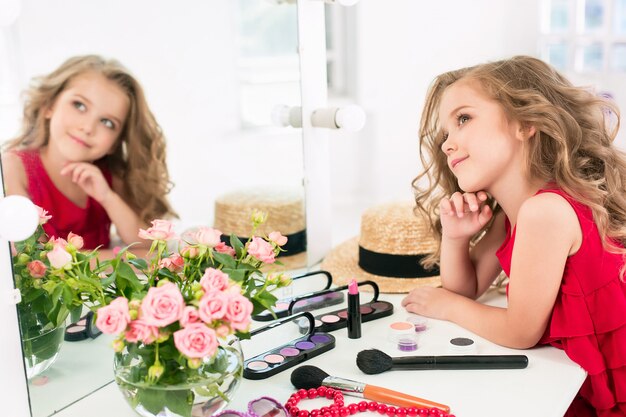 Une petite fille avec une robe rouge et des cosmétiques.