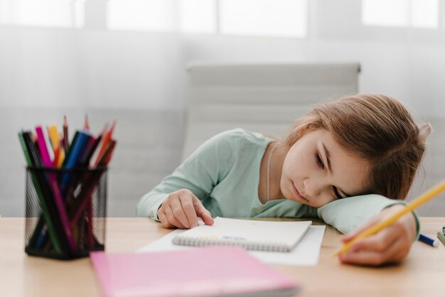 Petite fille s'ennuie à prendre des notes tout en ayant un cours en ligne