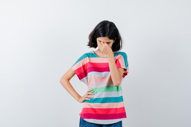 Petite fille se frottant les yeux et le nez en t-shirt et l'air fatigué, vue de face.