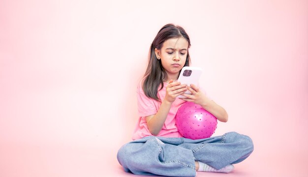 Petite fille avec un smartphone dans ses mains sur un espace de copie de fond rose