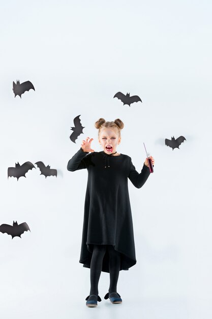 Petite fille sorcière en robe longue noire et accessoires magiques. Halloween.