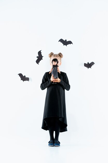 Petite fille sorcière en robe longue noire et accessoires magiques. Halloween