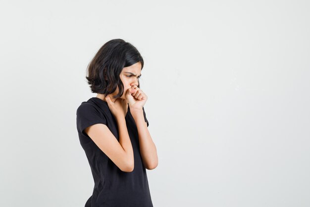 Petite fille souffrant de toux en t-shirt noir et à la recherche de malade. vue de face.