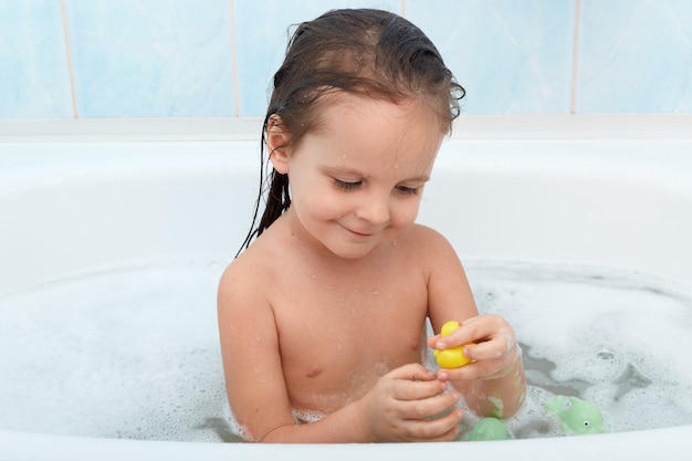 Petite fille souriante prenant un bain et jouant avec des jouets.