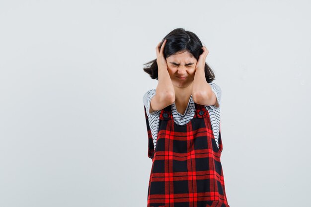 Petite fille en t-shirt, combinaison serrant la tête avec les mains et à la recherche de stress,