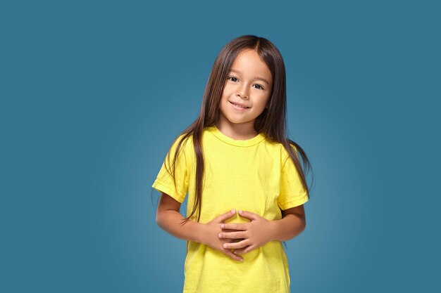 Petite fille en t-shirt jaune sourit sur fond bleu