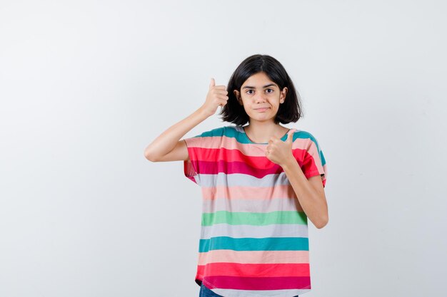 Petite fille en t-shirt montrant le double pouce vers le haut et l'air heureux, vue de face.