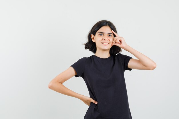Petite fille en t-shirt noir debout dans la pensée pose et à l'optimiste, vue de face.
