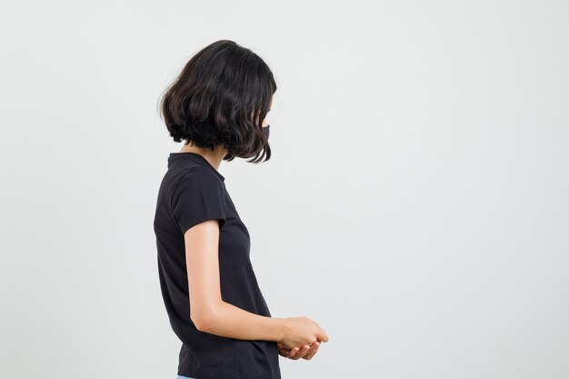 Petite fille en t-shirt noir, masque debout et à la recherche de calme.