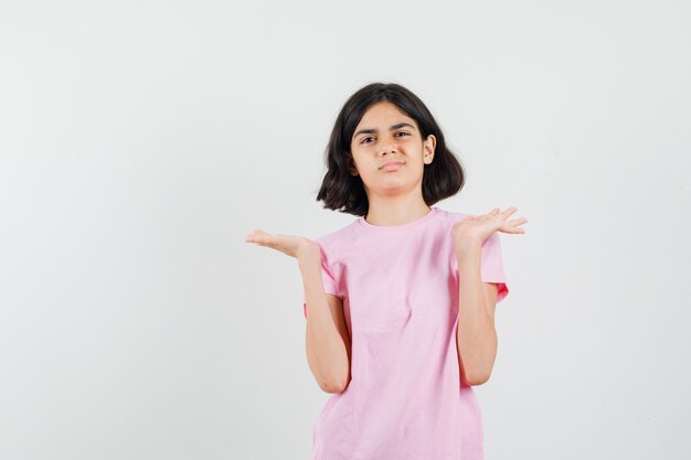 Petite fille en t-shirt rose faisant des gestes comme montrer ou tenir quelque chose et à la recherche de mécontentement, vue de face.