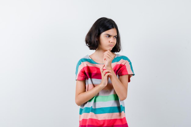 Photo gratuite petite fille en t-shirt serrant le poing, tenant la main sur le bras, regardant ailleurs et l'air mécontent, vue de face.