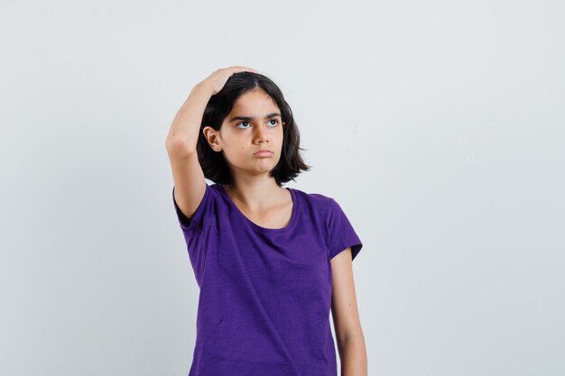 Petite fille en t-shirt tenant la main sur la tête et à la recherche désespérée,