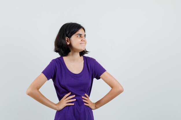 Petite fille en t-shirt tenant les mains sur la taille et à la recherche de plaisir,