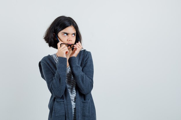 Petite fille en t-shirt, veste décollant des lunettes et à la douteuse,