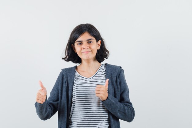 Petite fille en t-shirt, veste montrant deux pouces vers le haut et à la confiance