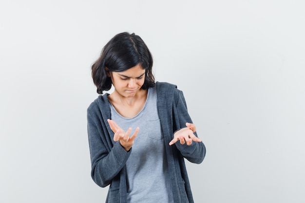 Petite fille en t-shirt, veste montrant un geste impuissant et à la réflexion