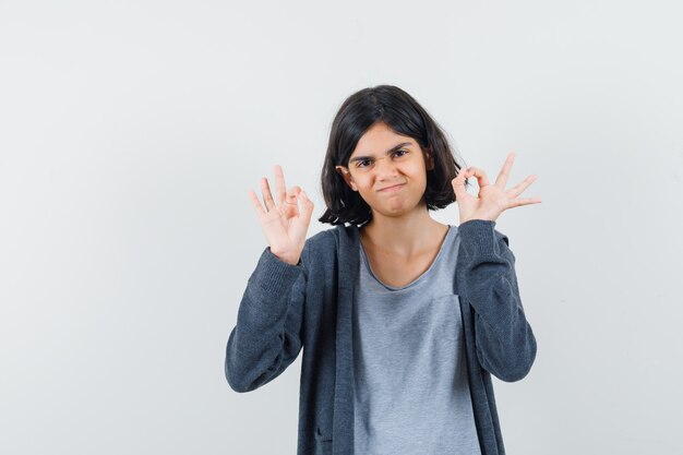 Petite fille en t-shirt, veste montrant le geste ok et à la confiance,