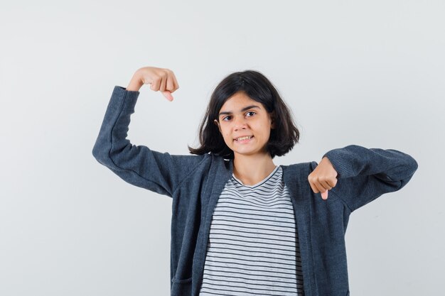 Petite fille en t-shirt, veste montrant les muscles des bras et à la confiance,