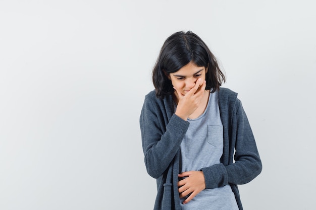 Petite fille en t-shirt, veste tenant la main sur la bouche et à la rêveuse