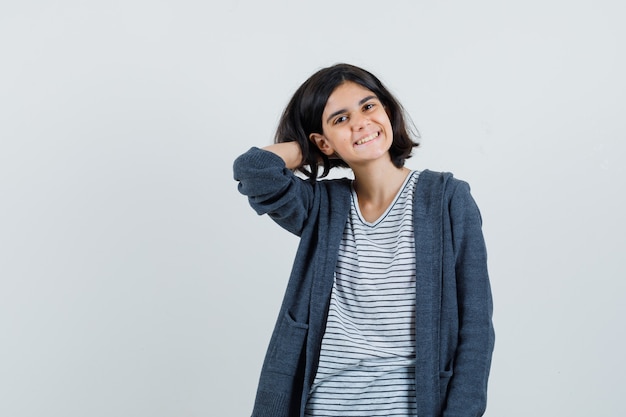 Petite fille en t-shirt, veste tenant la main sur le cou et à la bonne humeur,