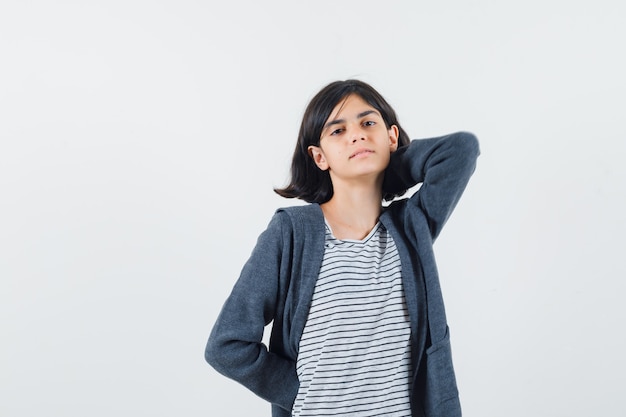 Petite fille en t-shirt, veste tenant la main sur le cou et à la détente