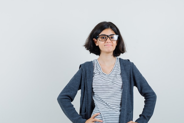 Petite fille en t-shirt, veste tenant les mains sur la taille et à la joie,