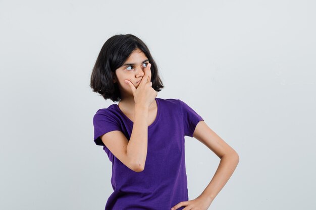 Petite fille tenant la main sur la bouche en t-shirt et à la réflexion.