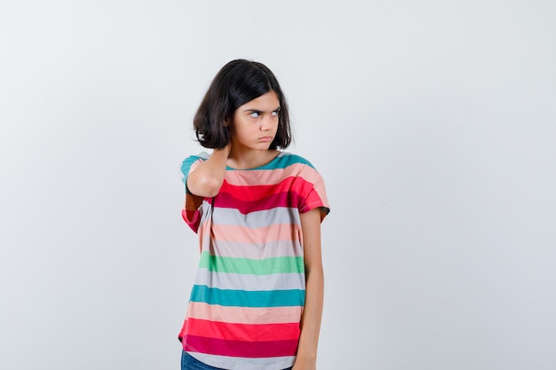 Petite fille tenant la main sur le cou, regardant loin en t-shirt et l'air mécontent, vue de face.