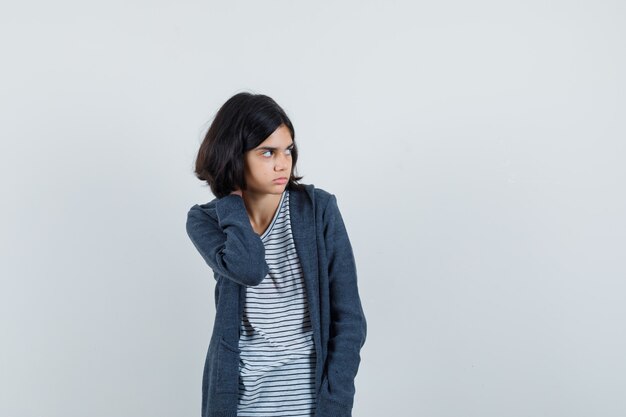 Petite fille tenant la main sur le cou en t-shirt, veste et à la pensif.