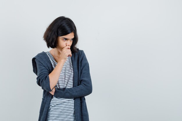 Petite fille tenant la main sur le menton en t-shirt, veste et à la pensif,