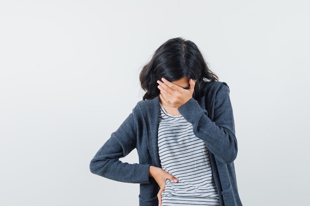 Petite fille tenant la main sur le visage en t-shirt, veste et à la déprimé