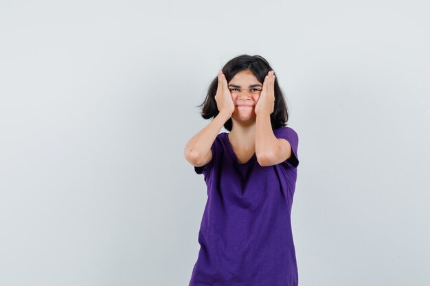 Petite fille tenant les mains sur les joues en t-shirt et à la recherche d'oubli,