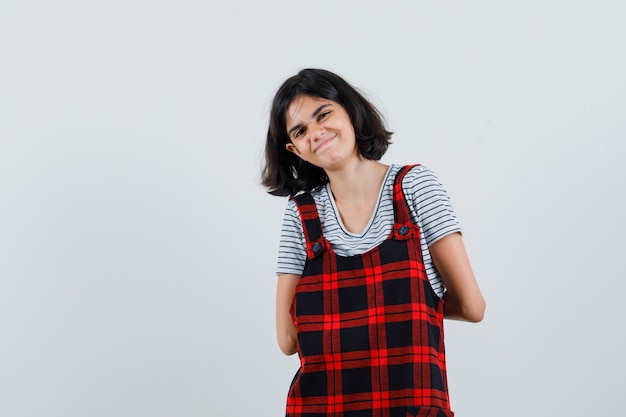 Petite fille tenant les mains sur sa colonne vertébrale en t-shirt, combinaison et à la joyeuse,