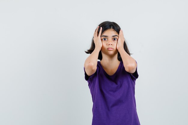 Petite fille tenant les mains sur la tête en t-shirt et à la perplexité.