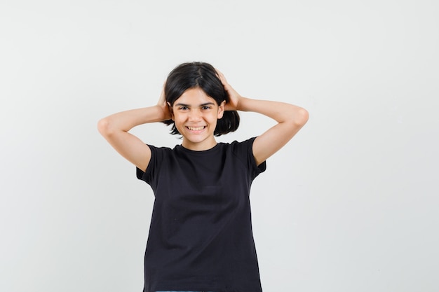 Petite fille tenant la tête avec les mains en t-shirt noir et l'air heureux. vue de face.