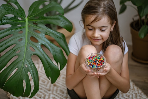 Petite fille tenant un vase avec des perles d'eau multicolores décoratives.