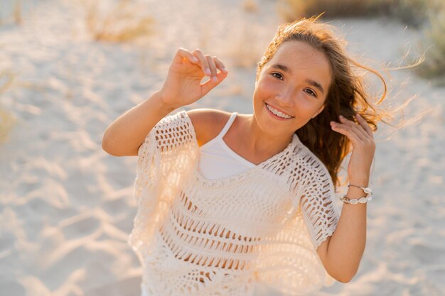 Petite fille en tenue boho élégante s'amusant et sautant sur la plage Couleurs chaudes du coucher du soleil Wacation et concept de voyage