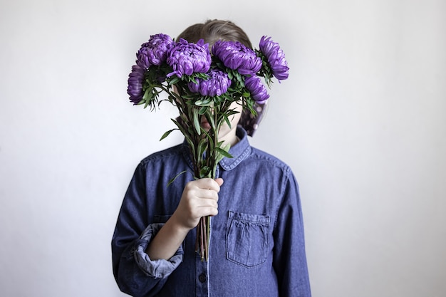 Une petite fille tient un bouquet de chrysanthèmes bleus dans ses mains.