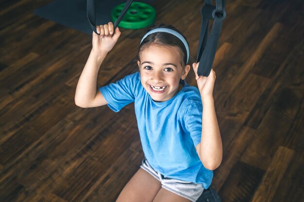 Photo gratuite petite fille utilisant des sangles de fitness trx pour travailler avec son propre poids