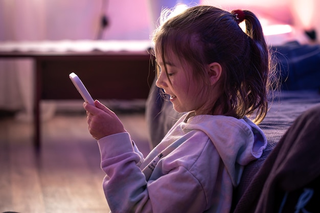 Une petite fille utilise un smartphone alors qu'elle est assise dans sa chambre