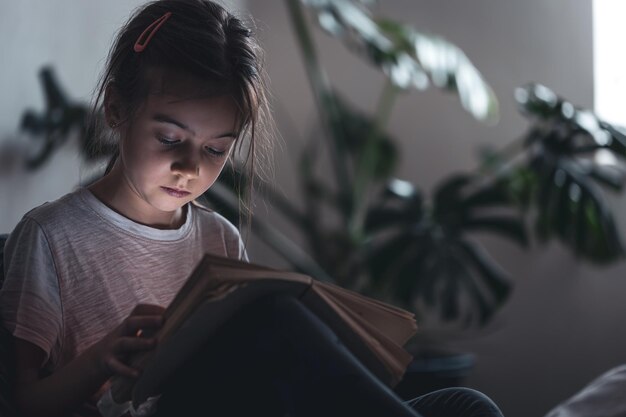 Une petite fille utilise le téléphone tenant un livre dans ses mains